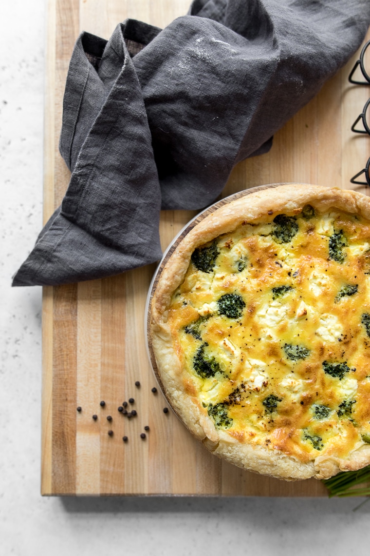 A freshly baked broccoli and cheese quiche on a wooden cutting board