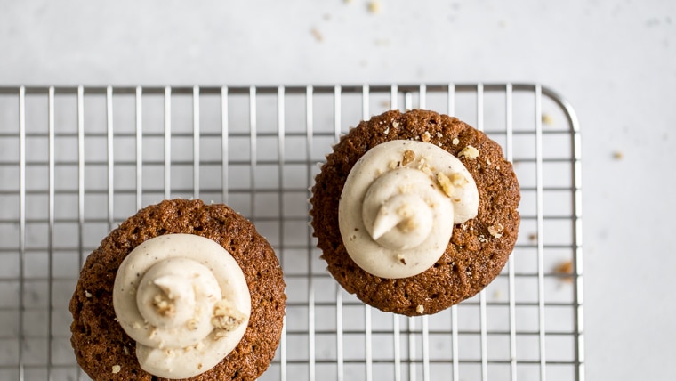 Two carrot cake muffins with frosting and crushed walnuts on a wire cooling rack