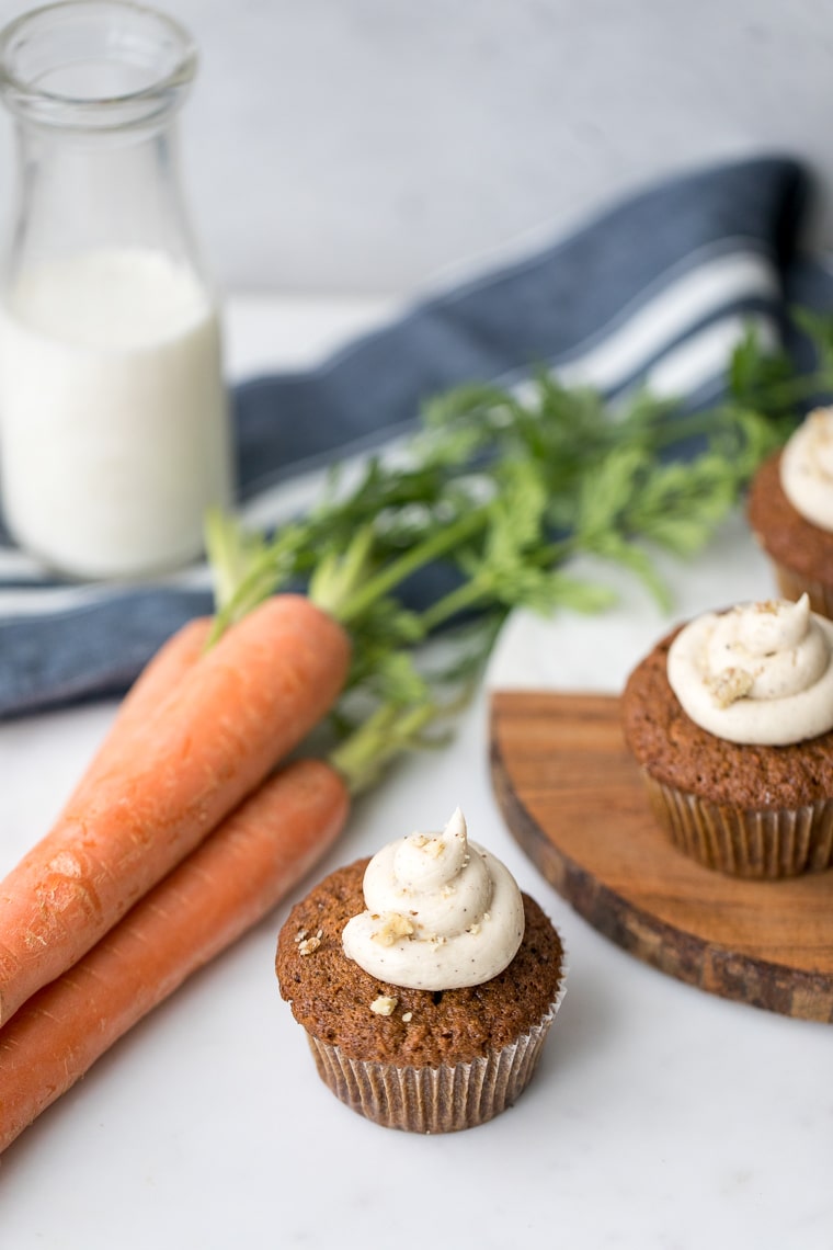 Carrot muffins with brown butter frosting next to fresh carrots and milk