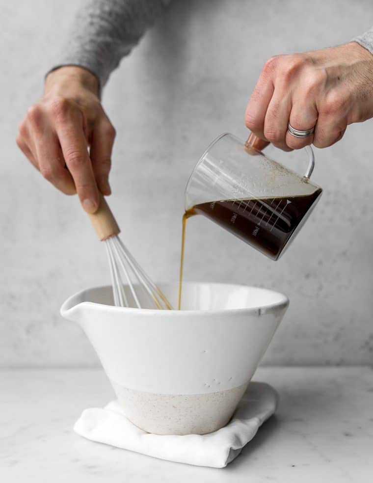Pouring brown butter from a measuring cup into a white bowl