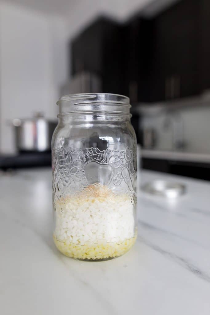 A mason jar with jojoba oil, beeswax pellets, and pine resin