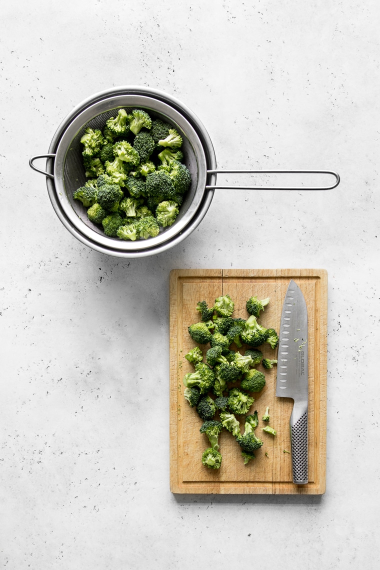 Cutting board with broccoli florets and knife next to a bowl with broccoli florets