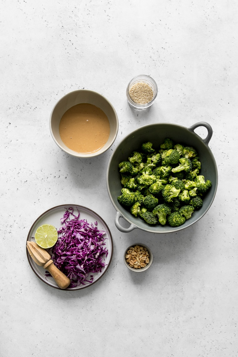 Bowl of Broccoli Florets, Plate with shredded red cabbage and lime half, peanut butter salad dressing, sesame seeds and peanuts