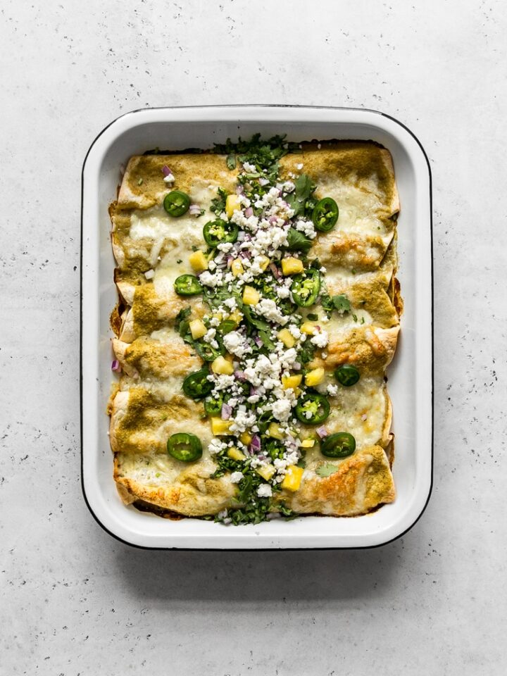 Freshly baked Pork Enchiladas Al Pastor with pineapple, jalapeños, red onion, cilantro and cheese on top