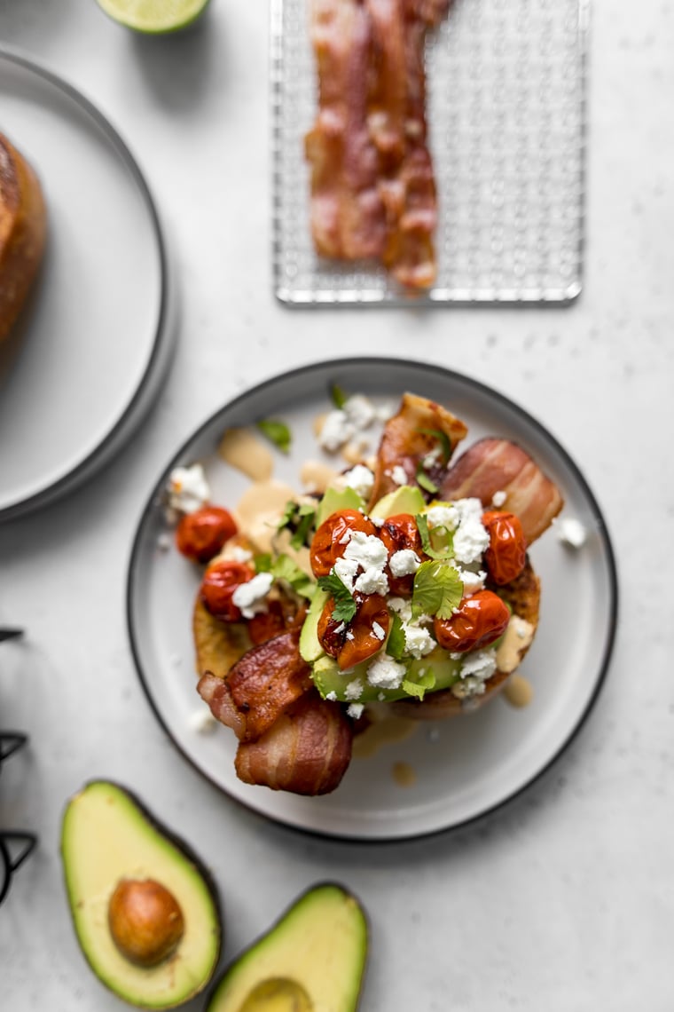Overhead view of Loaded French toast on a plate next to a cut avocado and bacon on a cooling rack