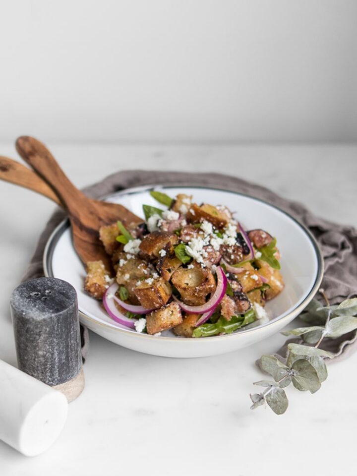 Fig Panzanella Salad in a bowl with tongs next to salt and pepper shakers
