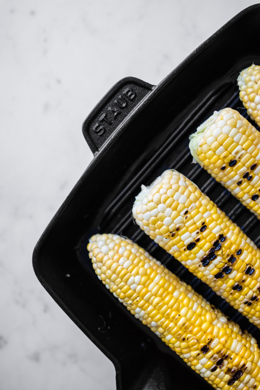 4 cobs of corn with char marks on a black grill pan 