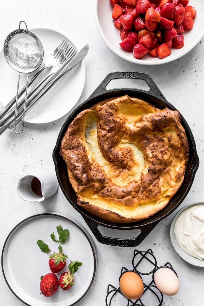 Plain dutch baby next to bowl of strawberries and maple whipped sour cream