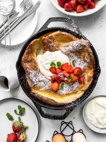 Dutch baby in cast iron skillet topped with strawberries and maple whipped sour cream