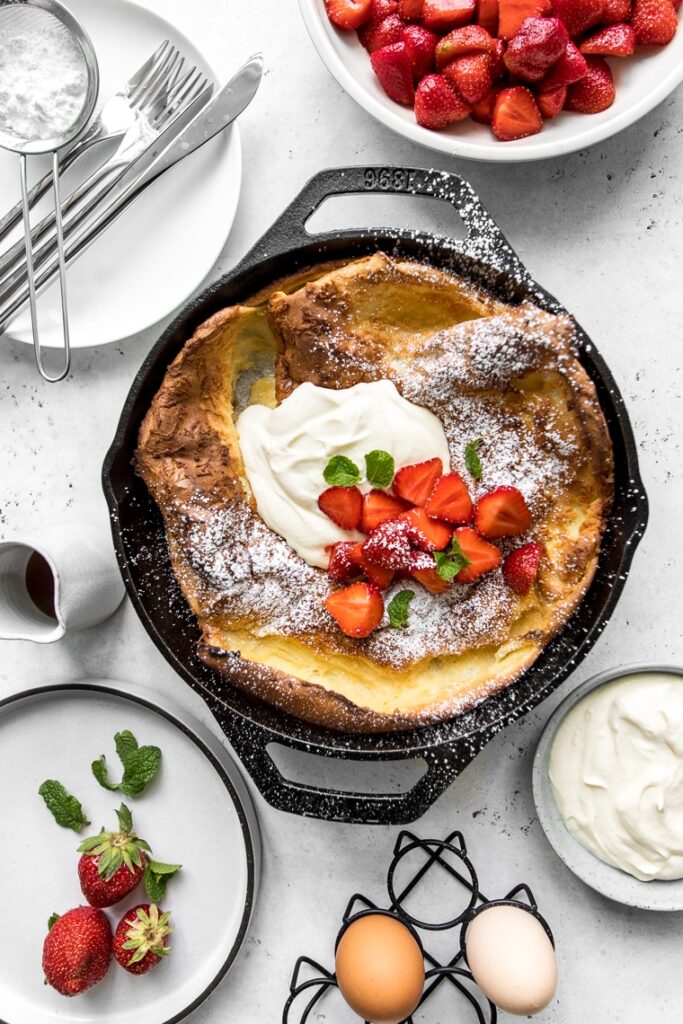 Dutch baby in cast iron skillet topped with strawberries and maple whipped sour cream