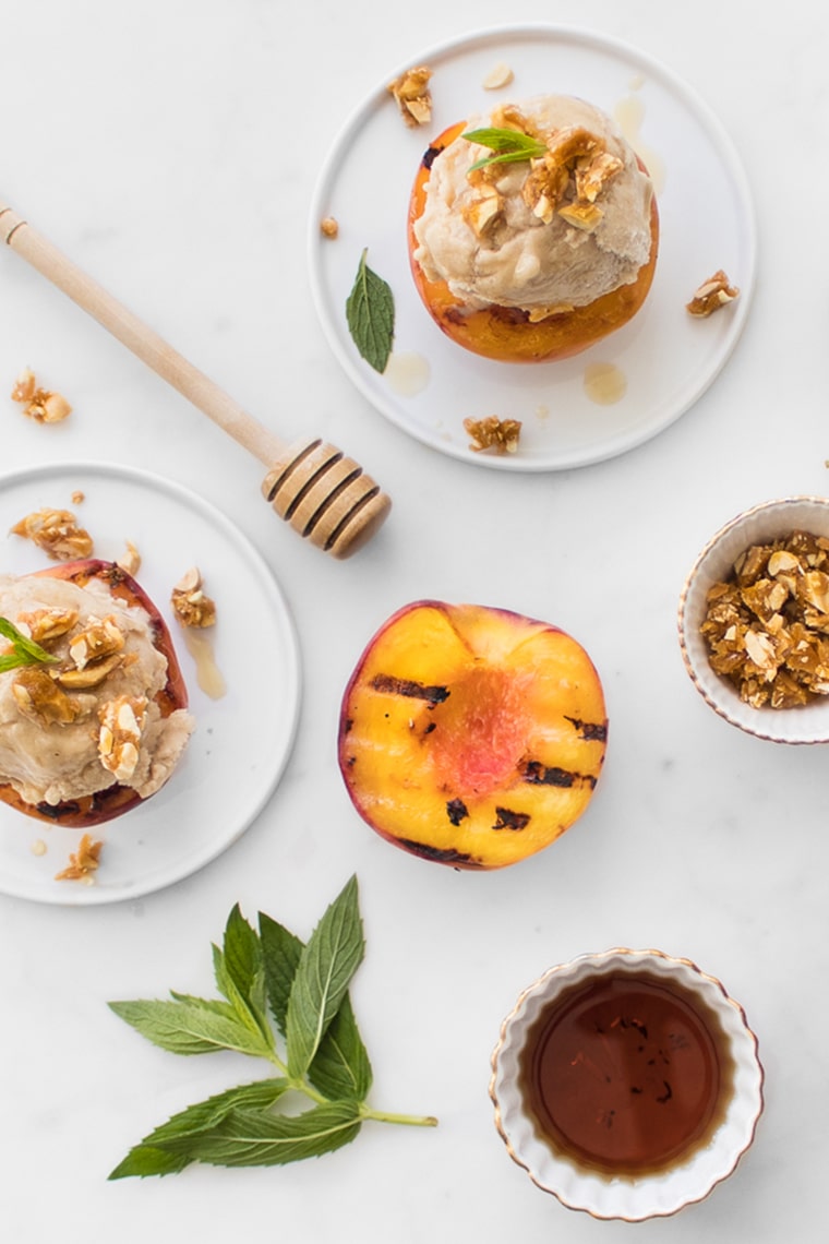 Flat Lay Image of Banana No-Churn Ice Cream on Grilled Peaches, Honey Stick and Bowl of Candied Nuts