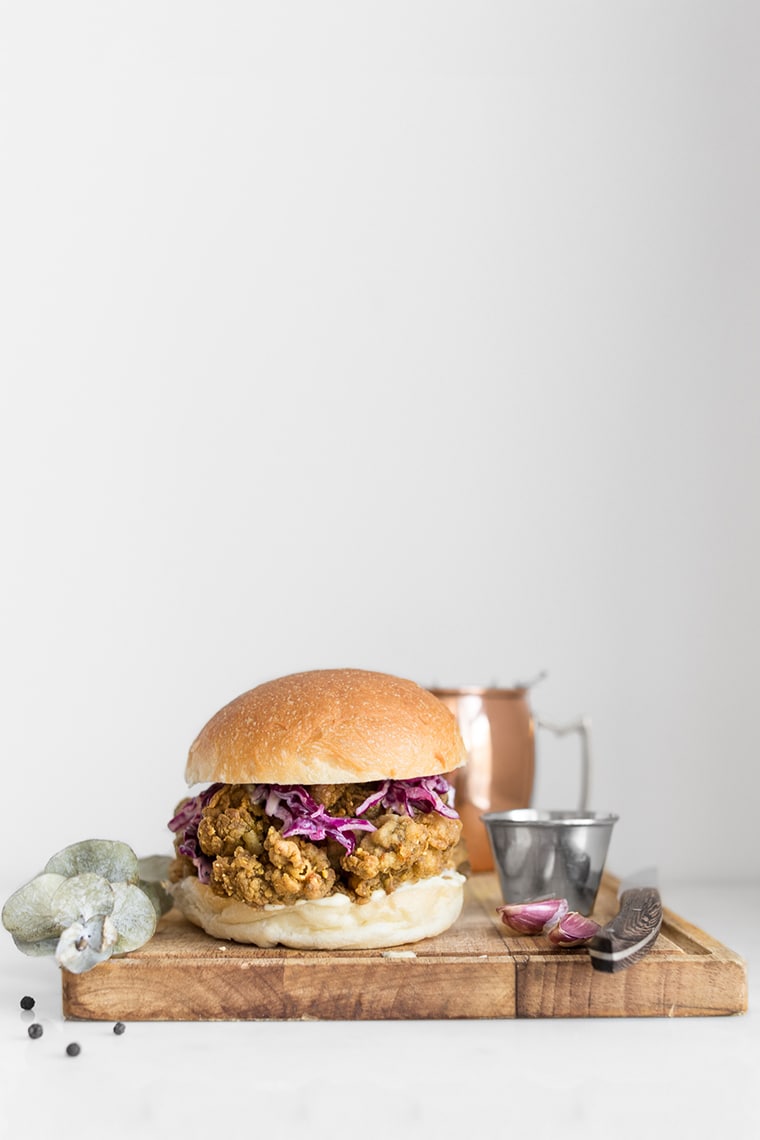 
Curry Fried Chicken Sandwich on a cutting board with eucalyptus, silver cup and knife