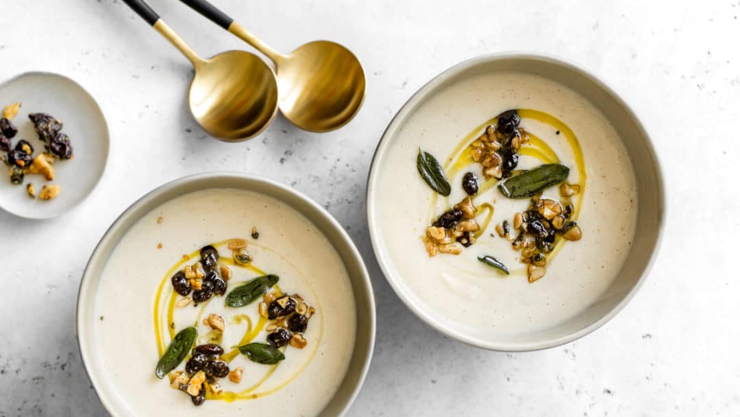 Two bowls of creamy cauliflower soup with two gold spoons