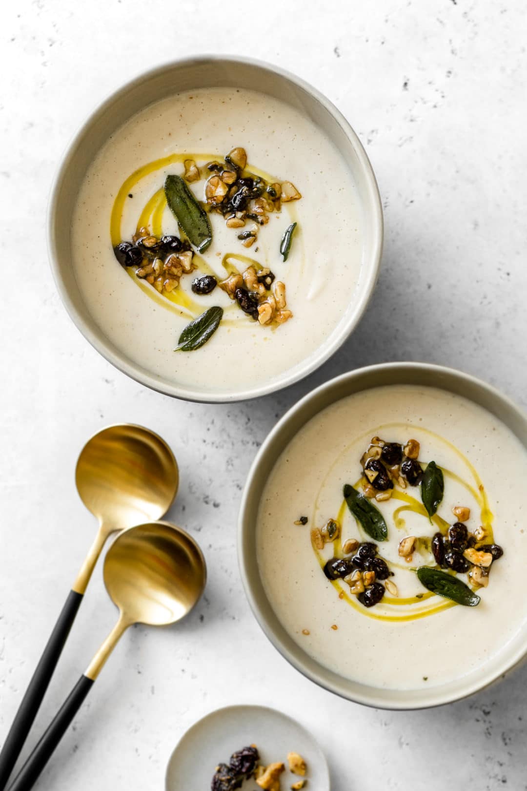 Two bowls of Cauliflower Soup with black and gold spoons