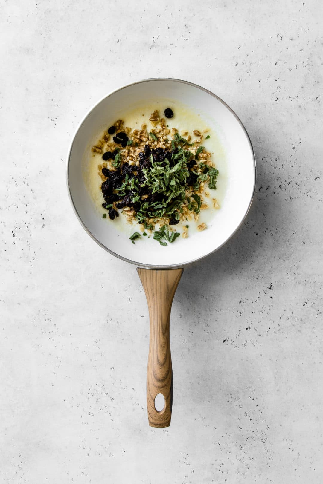 Walnuts, raisins, sage and olive oil in a white frying pan