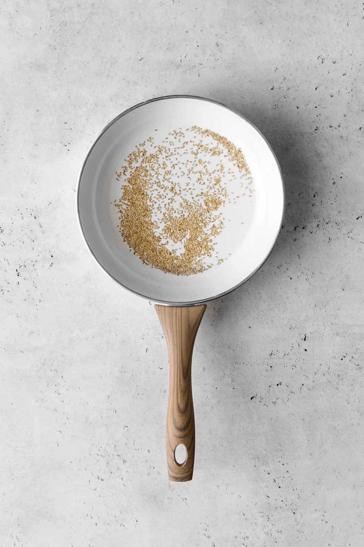 Sesame seeds being toasted in a white frying pan