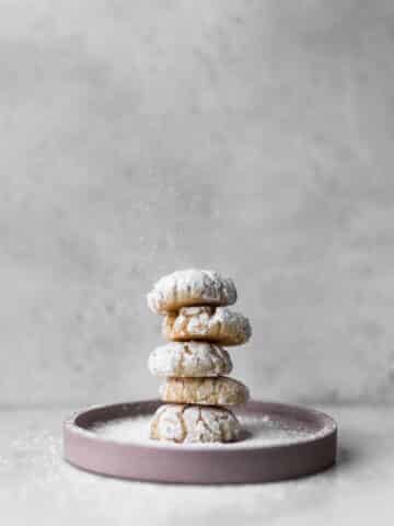 Five amaretti cookies stacked on a pink plate