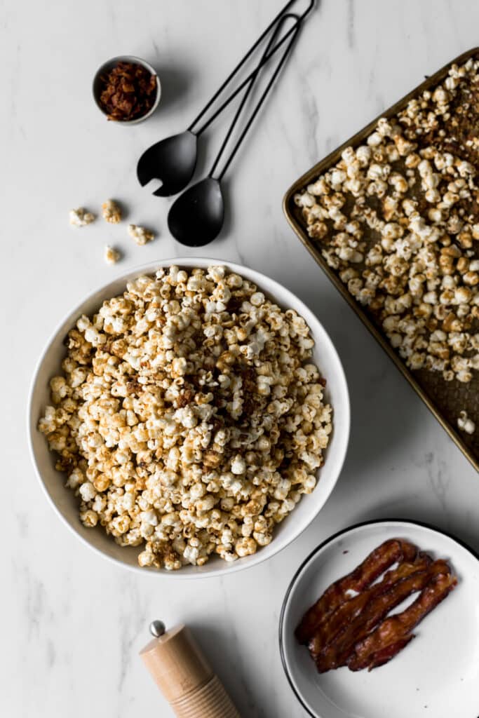 Bowl of maple and brown sugar popcorn with bacon, plate with bacon, black utensils