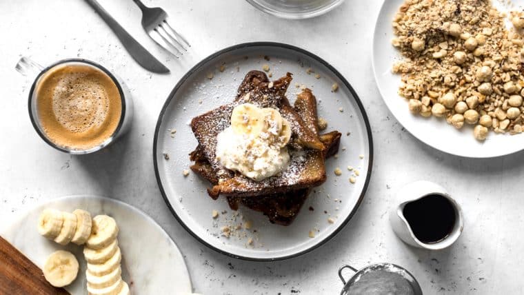 Coffee and Cinnamon French Toast with Whipped Cream surrounded by coffee, hazelnuts and sliced bananas