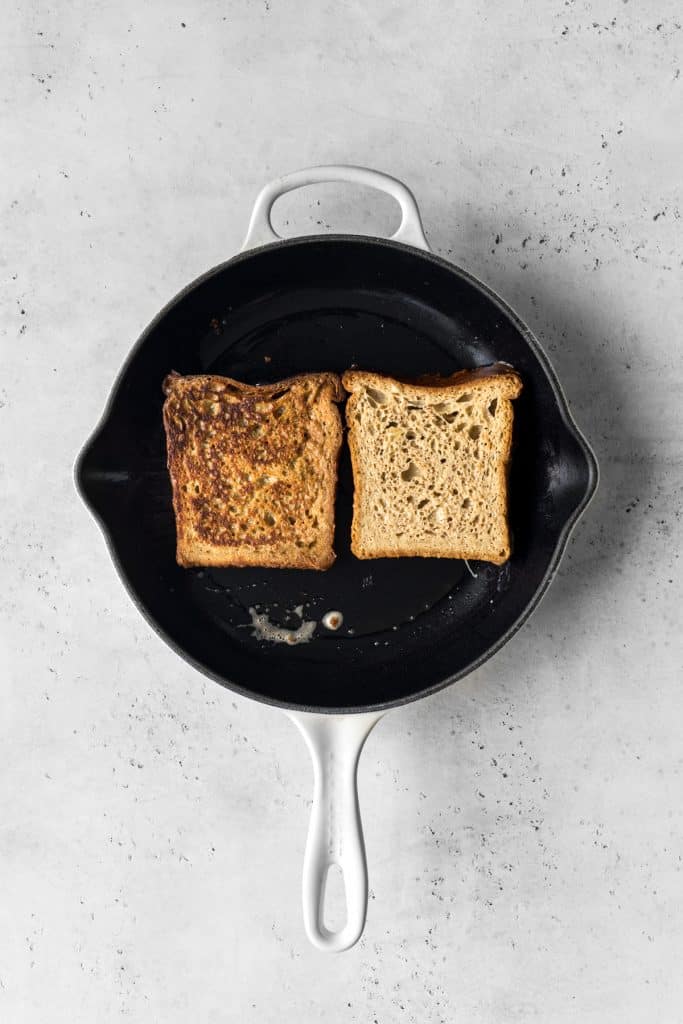 Two slices of french toast cooking in a Le Creuset cast iron skillet