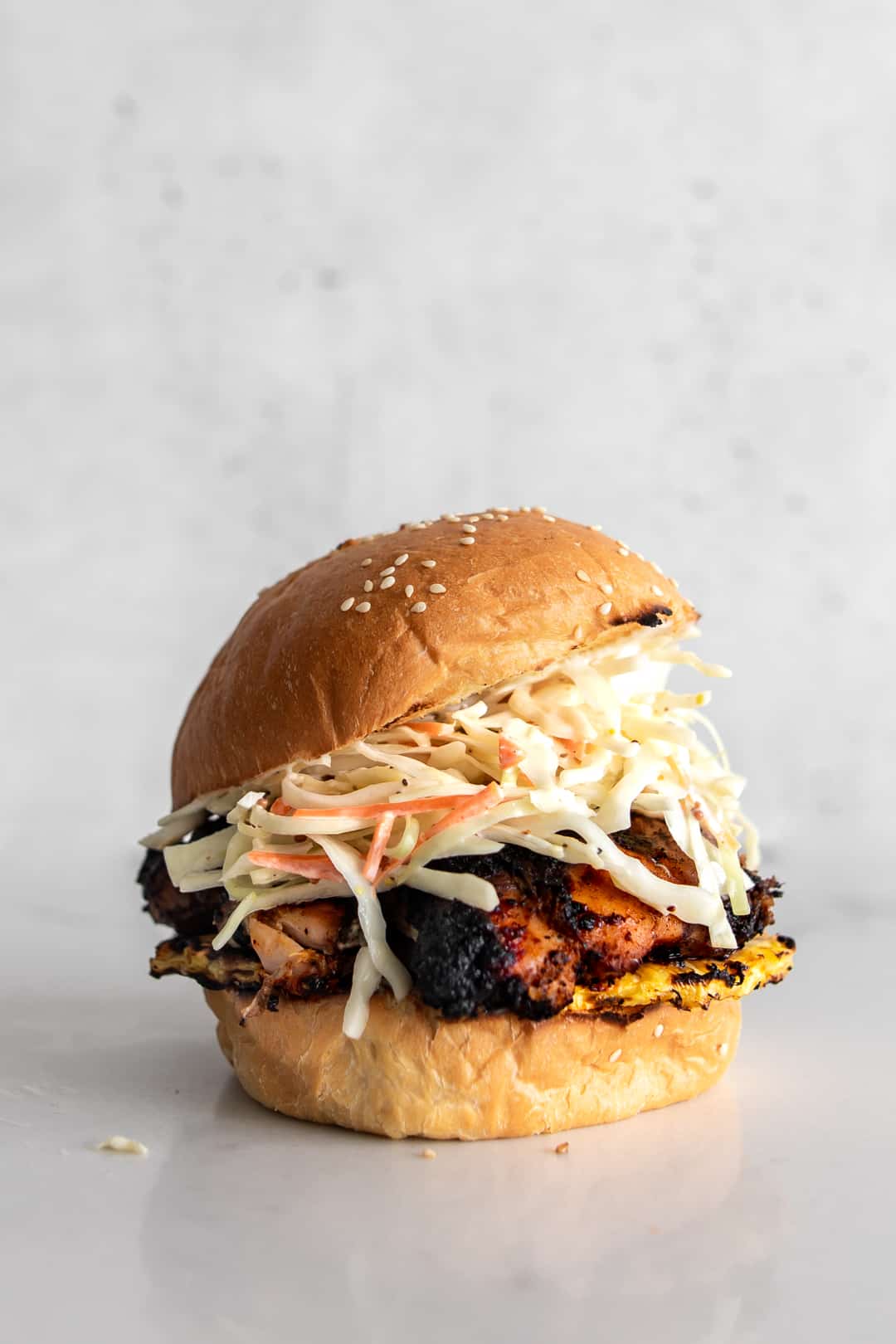 Closeup of bbq jerk chicken with grilled pineapple and simple coleslaw on a sesame seed bun