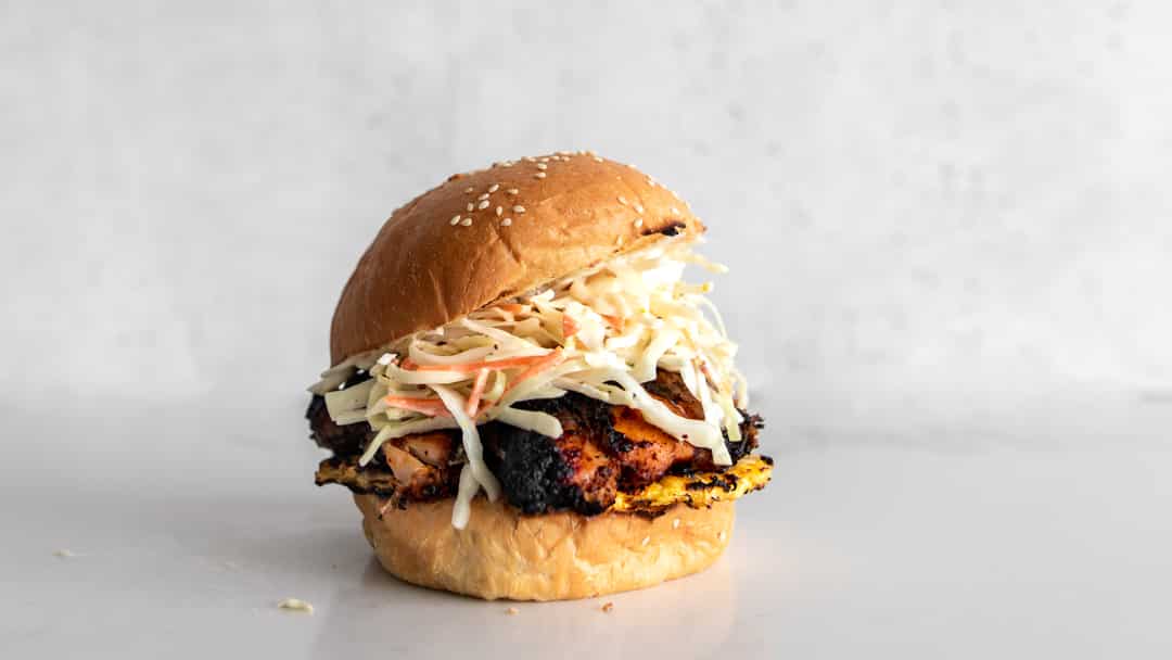 Jerk Chicken Sandwich with grilled pineapple and coleslaw on a sesame seed bun