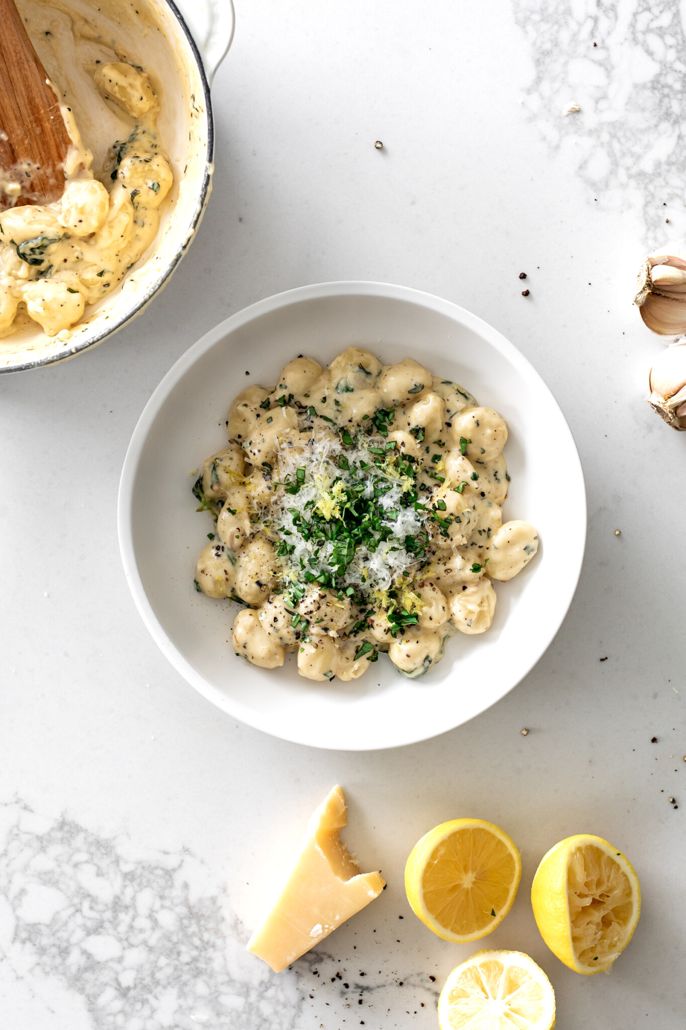 Creamy Lemon Gnocchi in a bowl with lemons, parmesan and garlic around it.