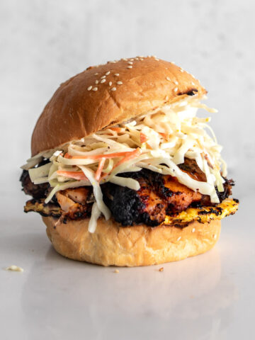 Grilled BBQ Jerk Chicken Sandwich on a sesame seed bun with grilled pineapple and coleslaw