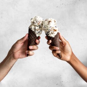 Hands holding chocolate waffle cone with no-churn ice cream with chocolate and pretzels