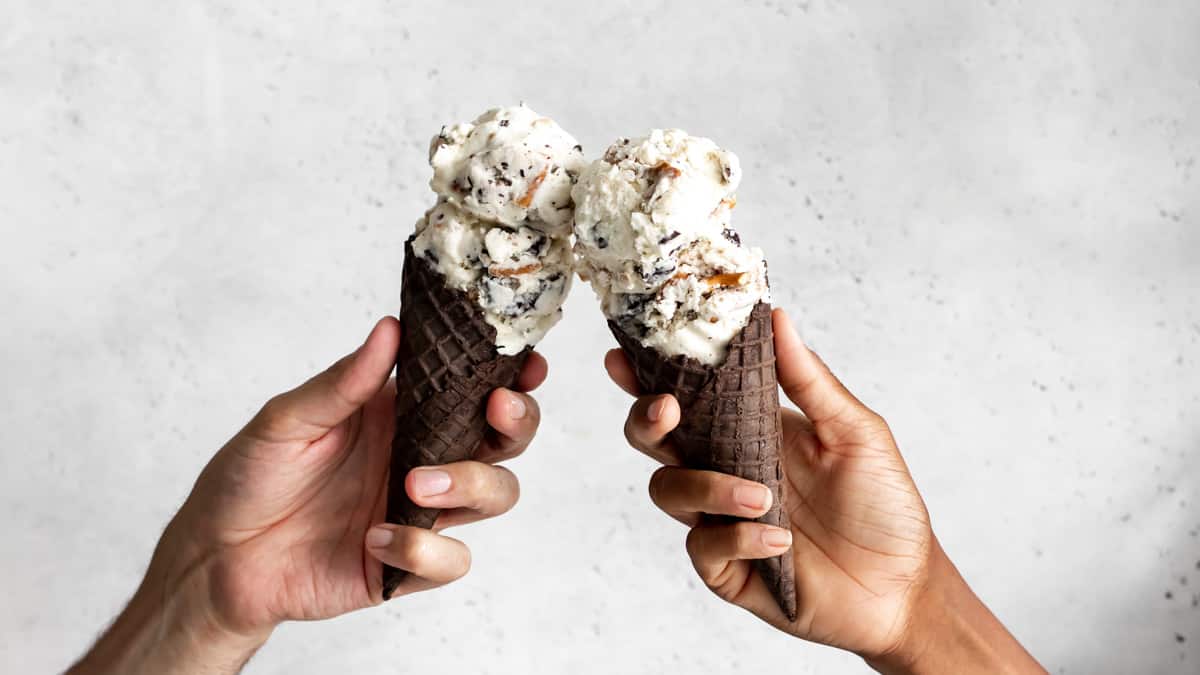Hands holding chocolate pretzel ice cream cones in chocolate waffle cone
