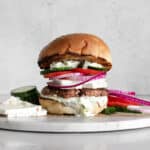 Greek Turkey Burger with Tzatziki, Feta Cheese, Red Onion, and Cucumbers on a marble board