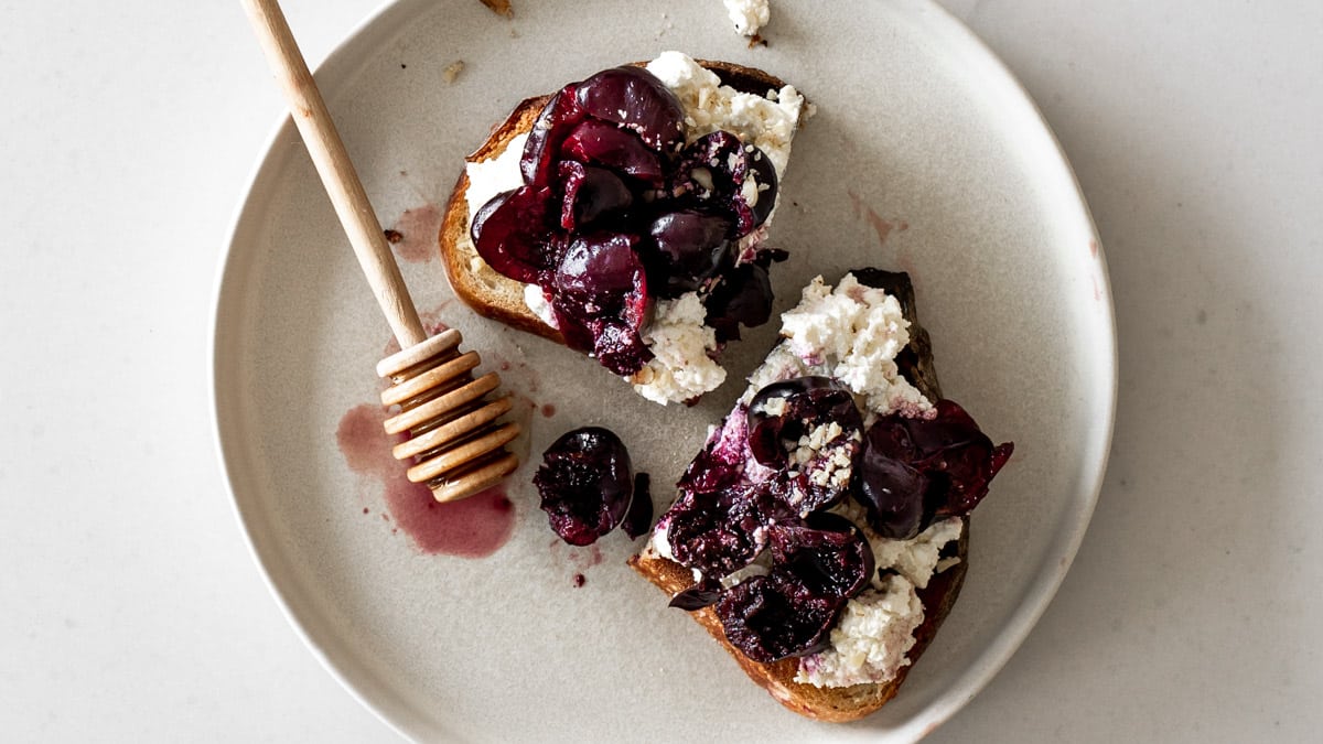 Ricotta Toast with Cherries on a plate with a honey dipper