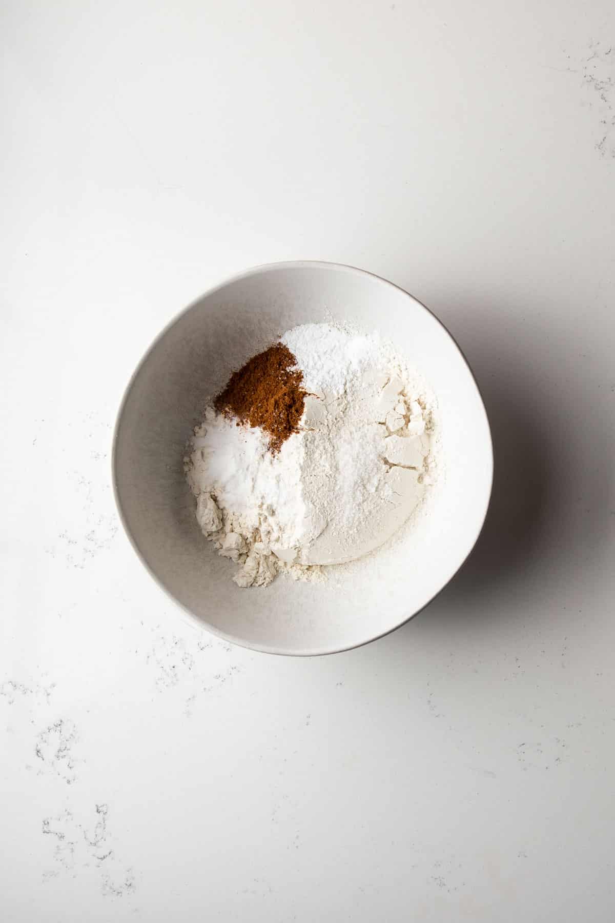 White bowl with flour, cinnamon, baking soda, baking powder and salt.
