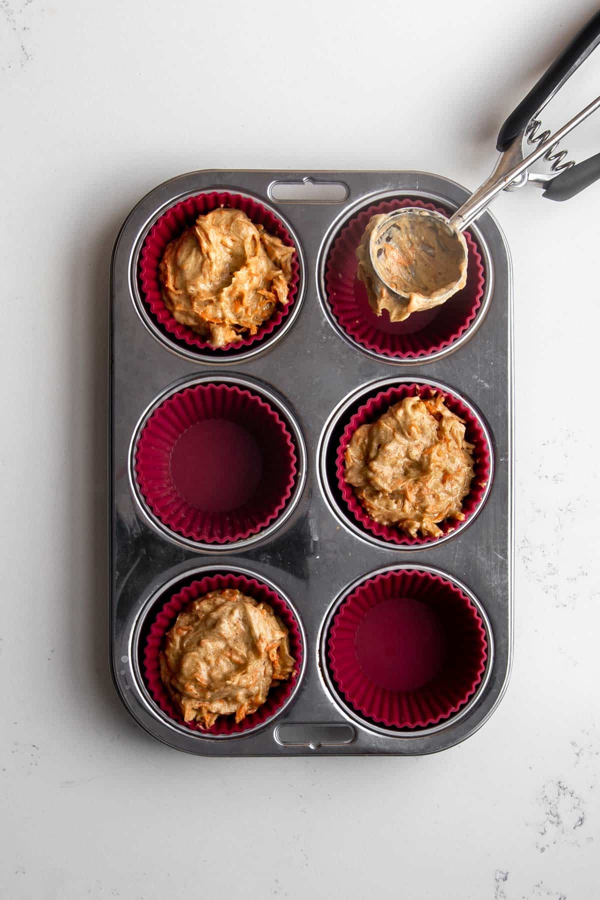 Muffin tin with red muffin liners, scoop and carrot cake muffin batter.