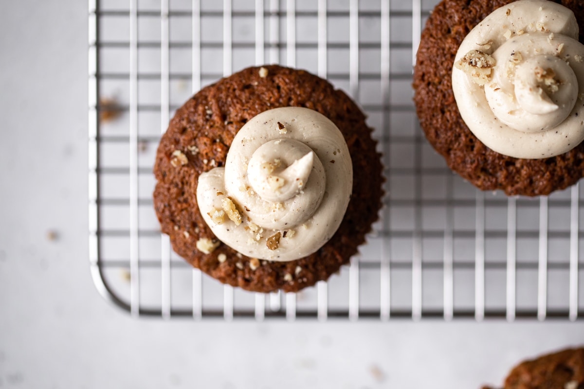 Carrot Cake Muffins with Brown Butter Frosting on a cooling rack with walnuts sprinkled overtop.