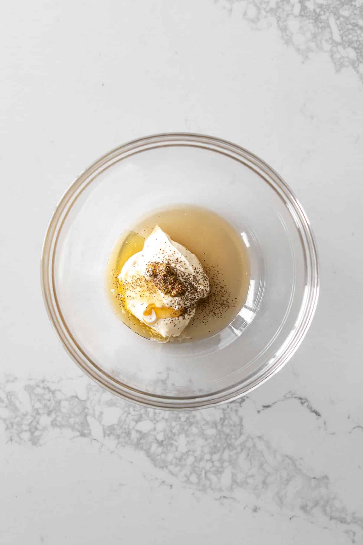 Mayonnaise, Dijon, honey, cider vinegar, celery seed, salt, and pepper in a clear bowl on a marble counter.