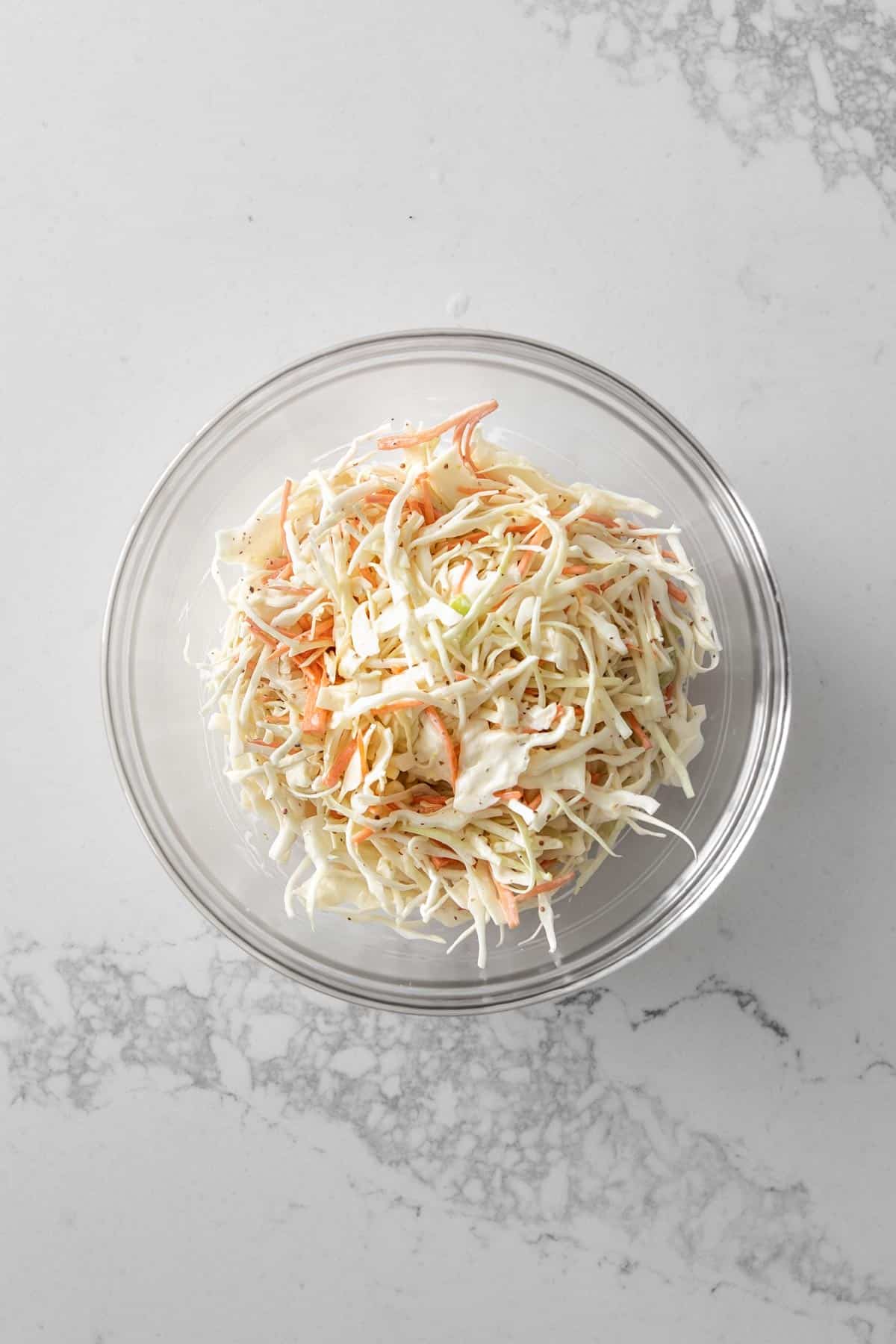 Creamy coleslaw in a glass bowl on marble countertop.