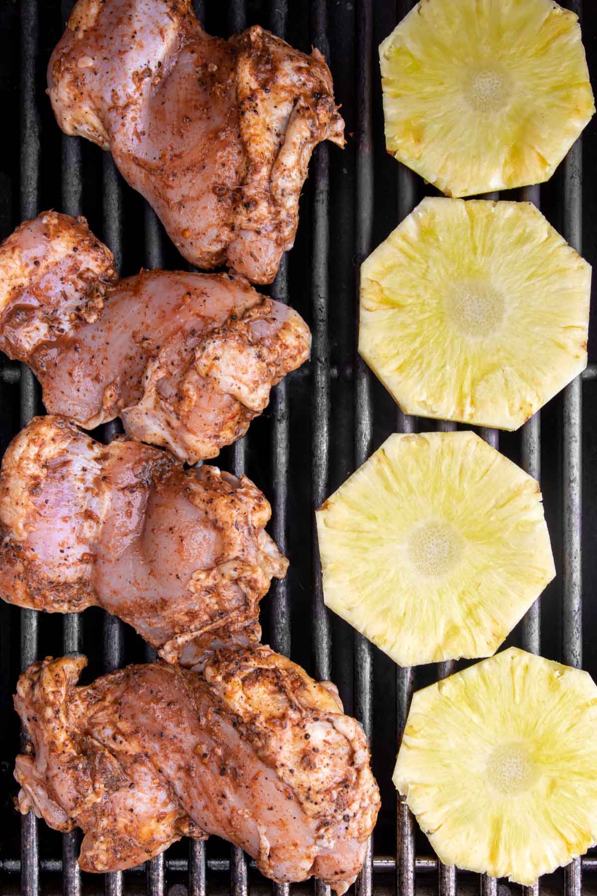 Jerk marinated chicken thighs and pineapple slices on barbecue grate.