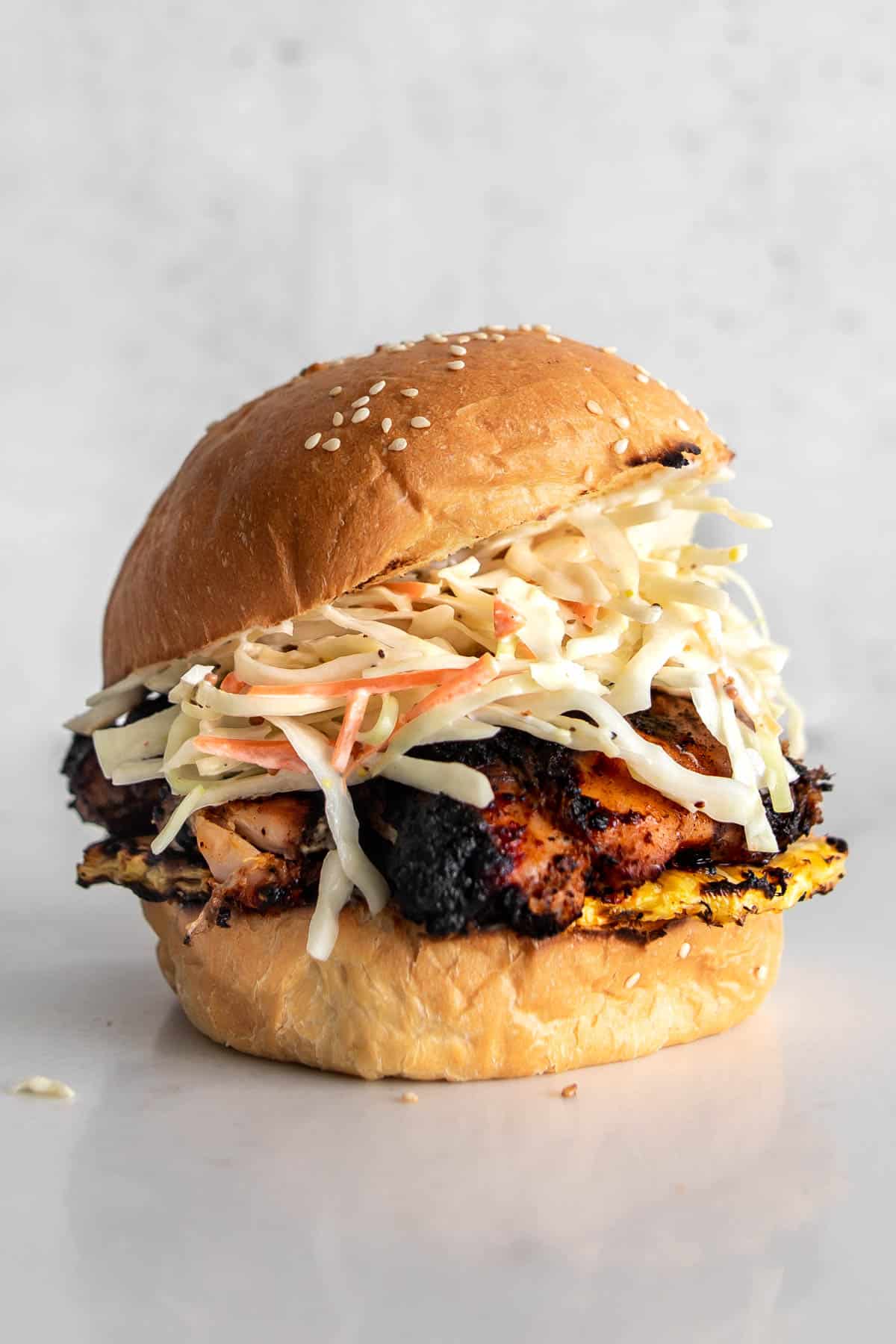 Grilled Jerk Chicken Sandwich with coleslaw and grilled pineapple on a sesame seed bun.