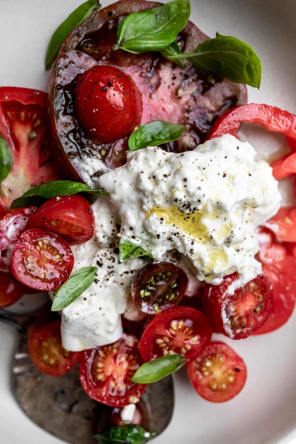 Serving of sliced heirloom and grape tomatoes, basil and burrata cheese on a grey plate.