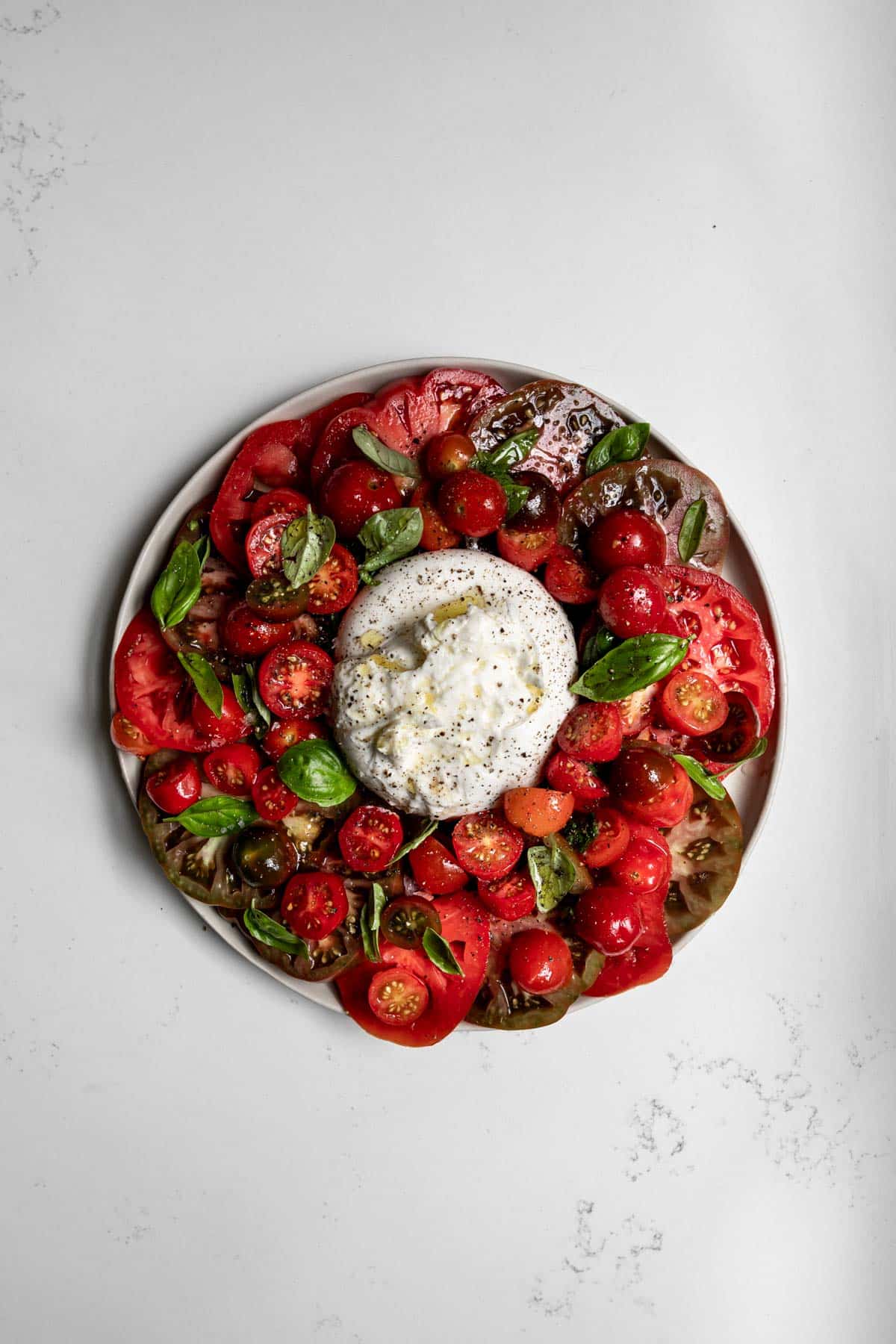 Burrata caprese salad on a white plate with white marble background.