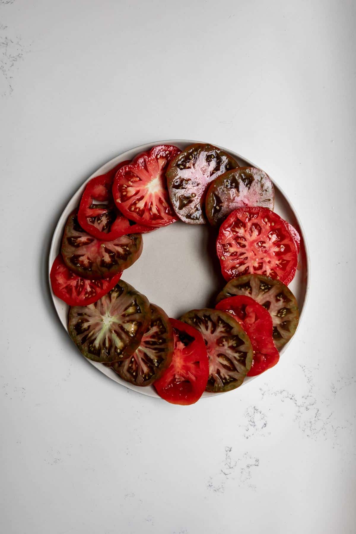 Sliced heirloom tomatoes arranged on the outer edge of a white plate. 