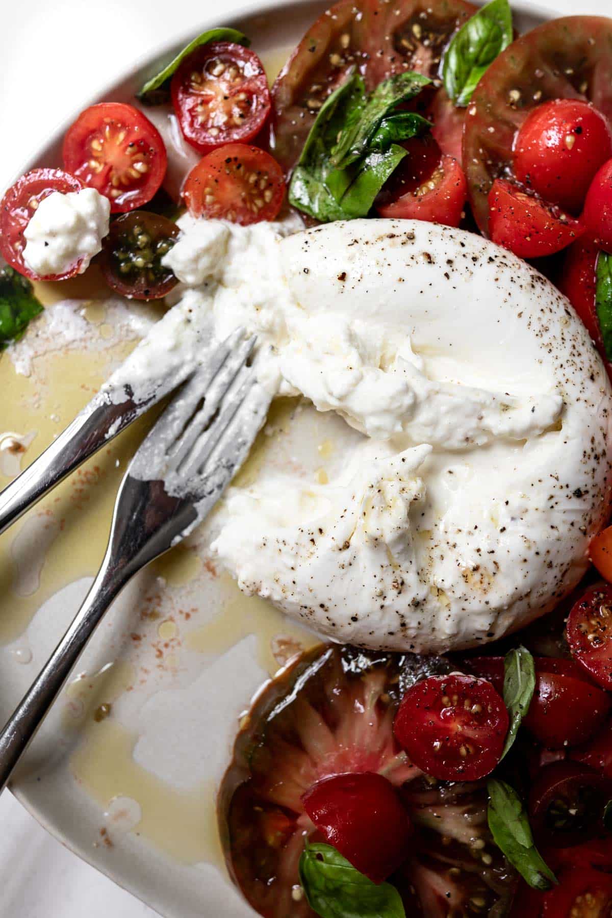 Burrata caprese partially eaten with fork and knife on a white plate. 