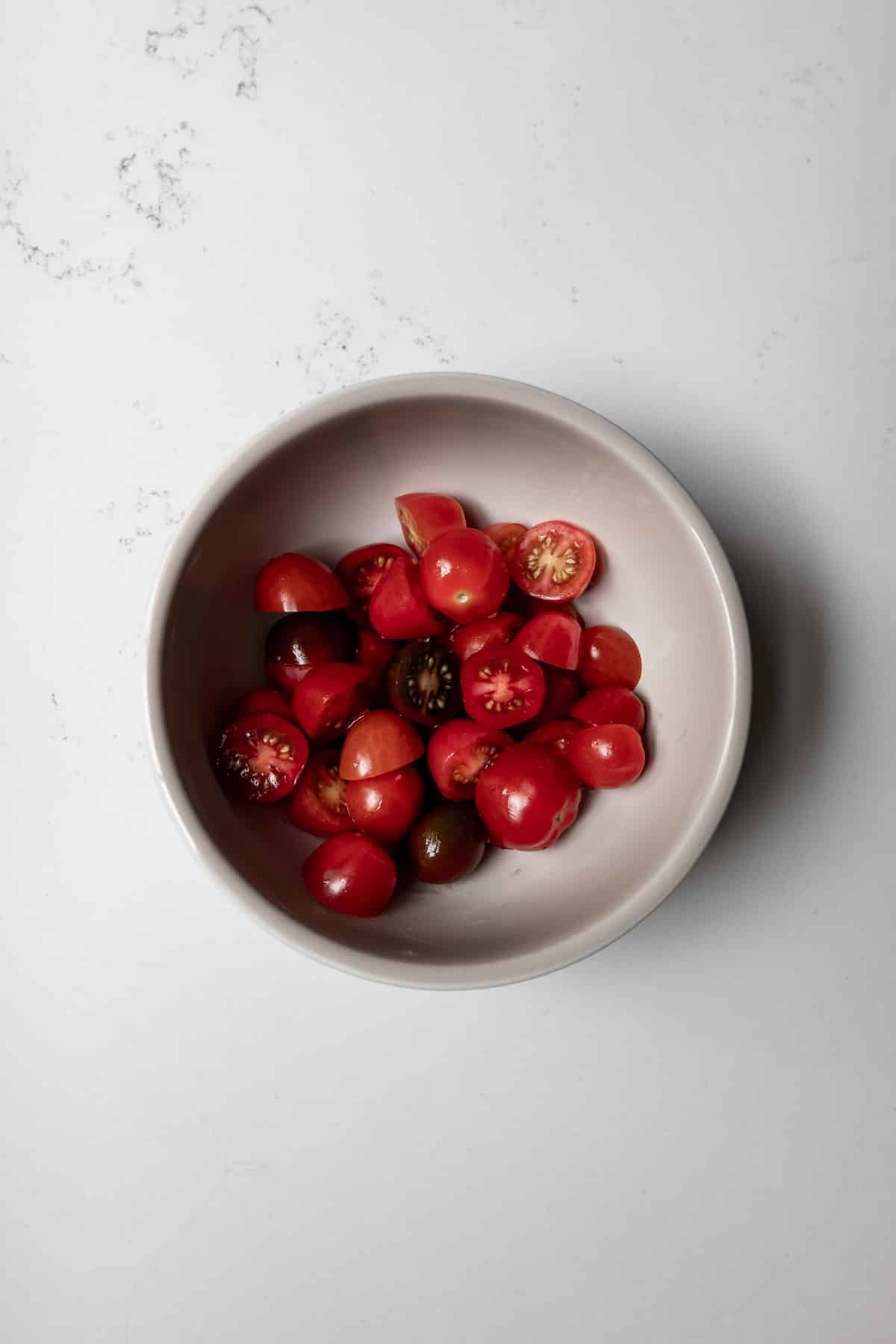 Grey bowl with halved grape tomatoes on a marble background. 