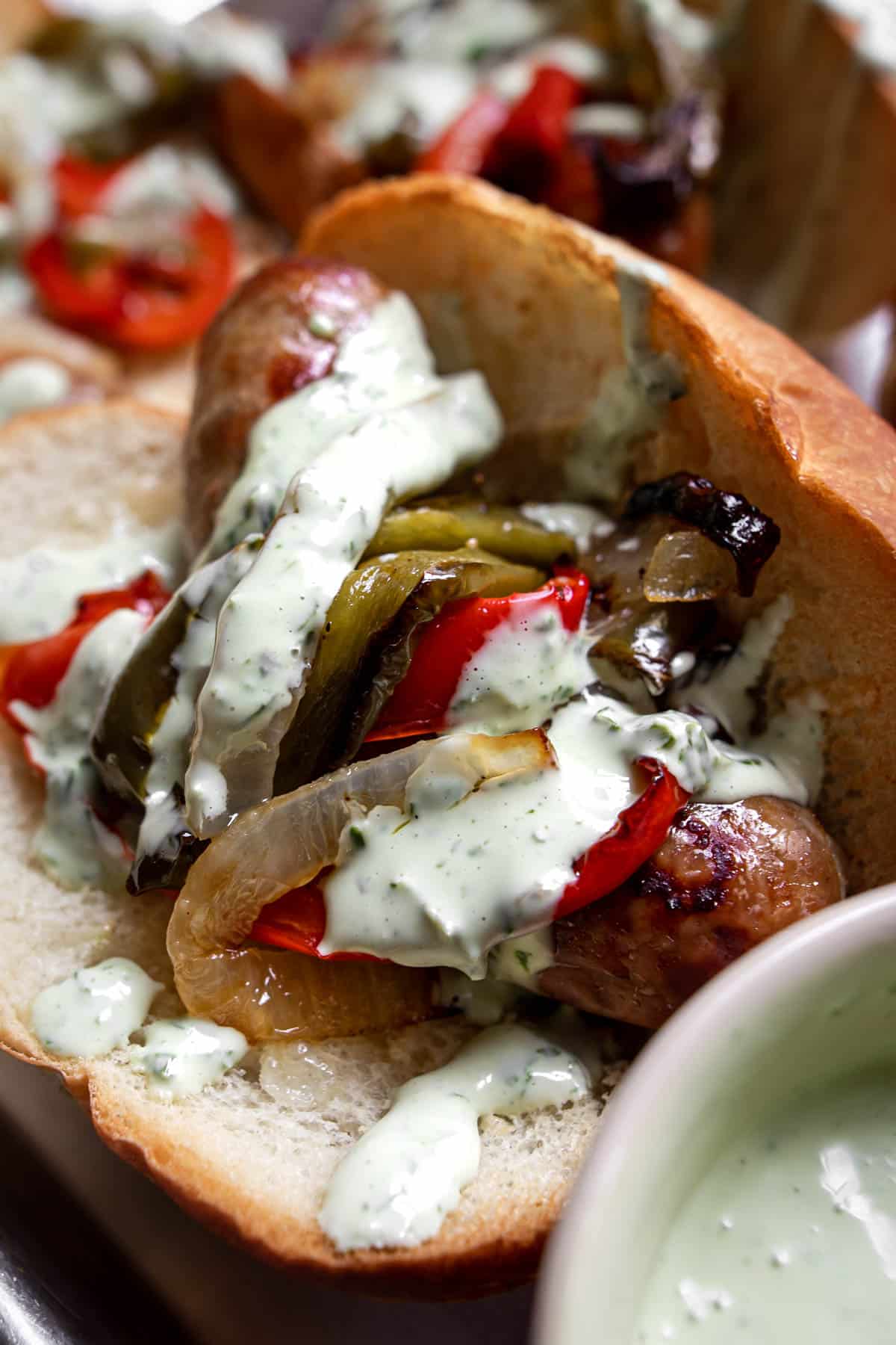 Sausage on a bun with basil mayo sauce and roasted peppers and onions.