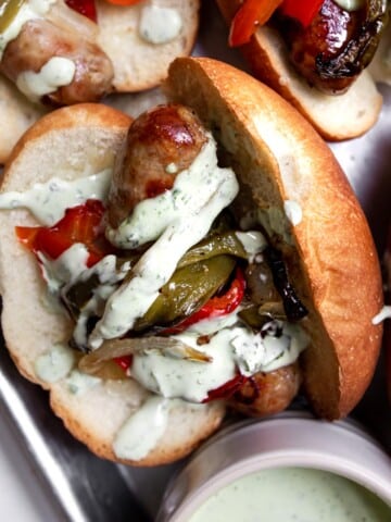 Italian sausage sandwich with roasted peppers and onions, drizzled with basil aioli.