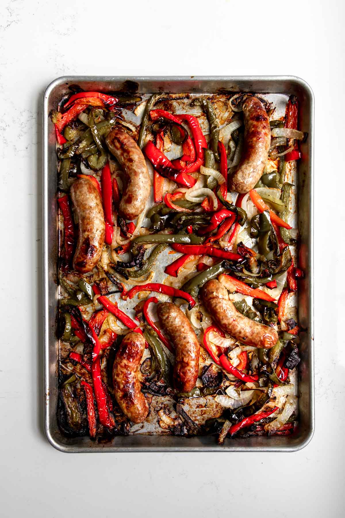 Roasted sausages, peppers, and onions on a baking sheet.