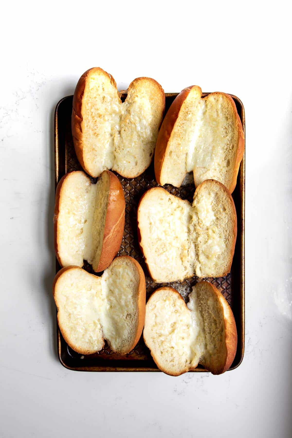 Toasted sausage buns with melted provolone cheese on a baking sheet.