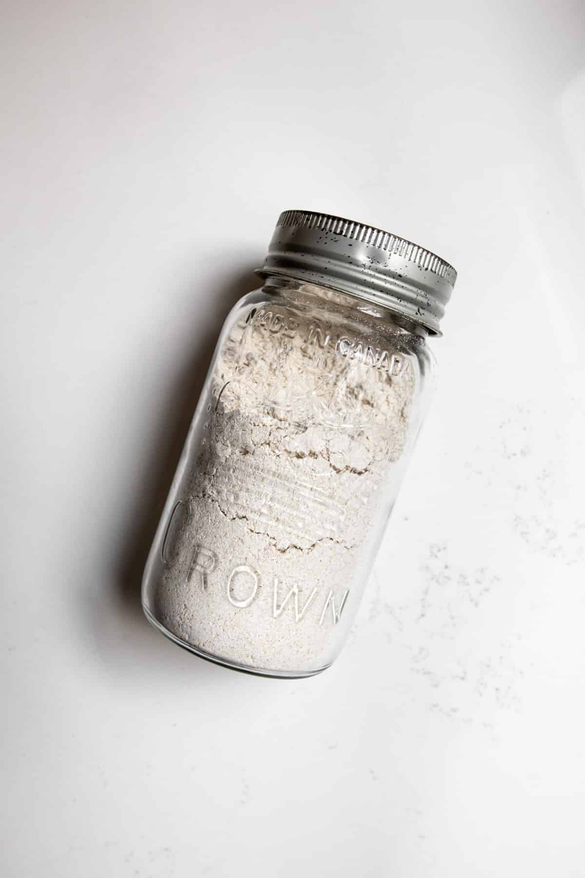 Large mason jar laying on counter with oat flour in it.