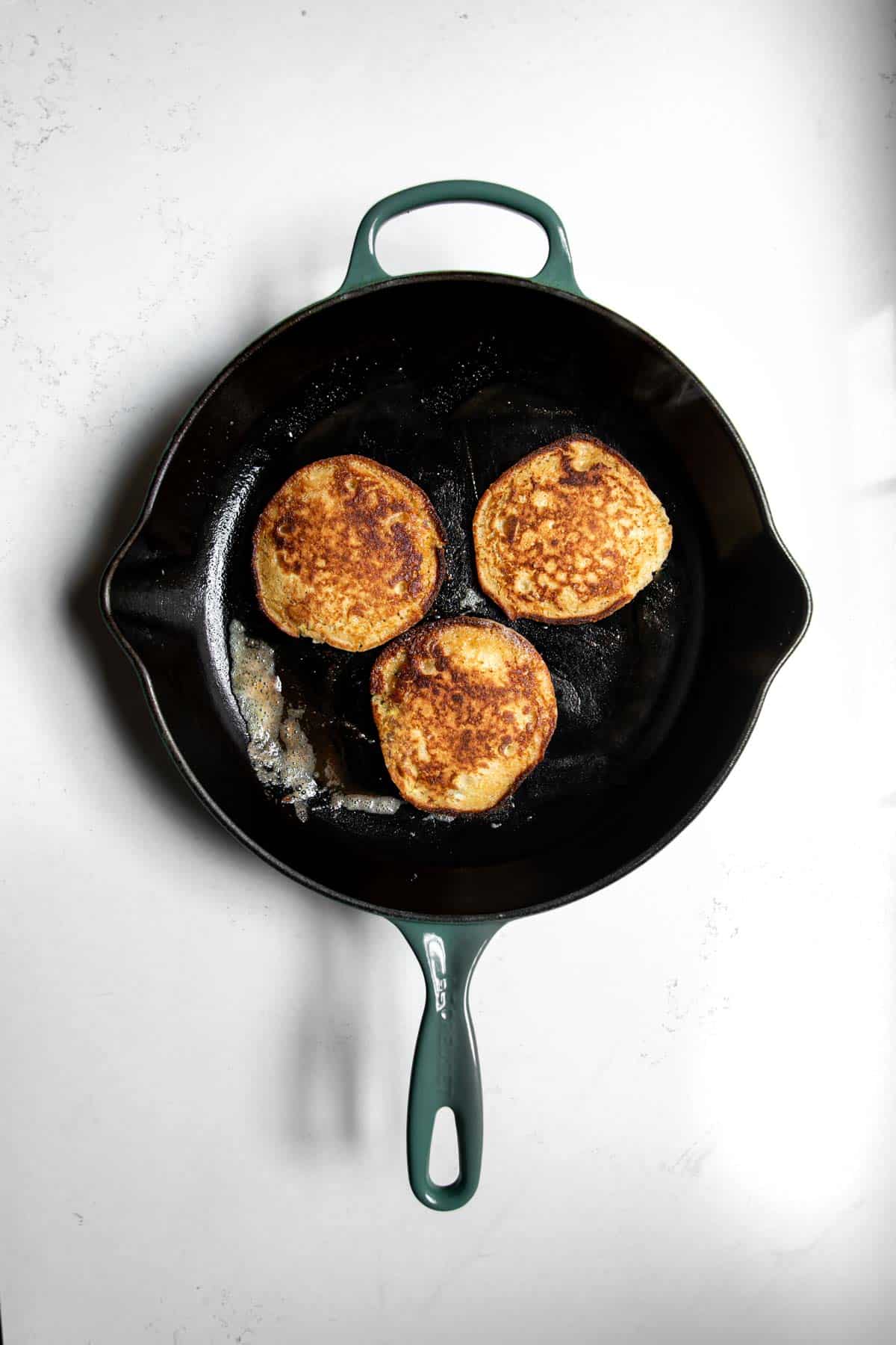 Three oat flour pancakes crispy and golden sitting on a skillet having been fully cooked.